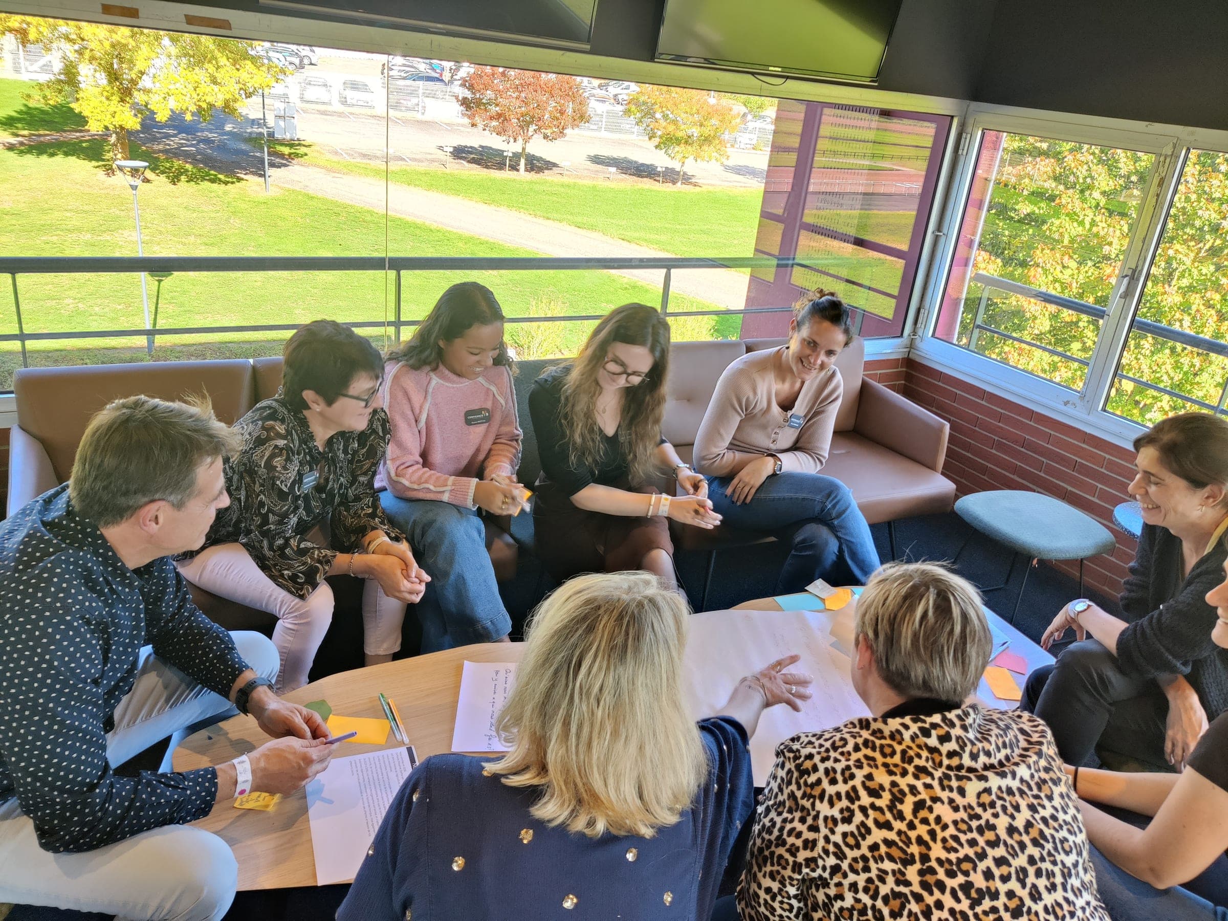 Un petit groupe travaille autour d’une table basse couverte de post-it, devant une baie vitrée